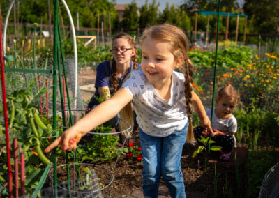 a girl reaches into a garden pointing excitedly at a green bean.