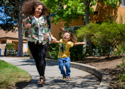 a you boy happily leaps and skips along side his mom with both of their hair flowing in the wind.